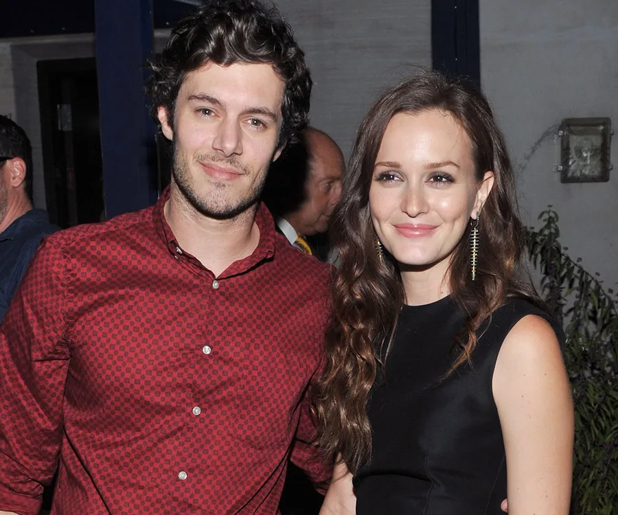 A man in a red shirt and a woman in a black dress smile together at an event.