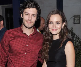 A man in a red shirt and a woman in a black dress smile together at an event.
