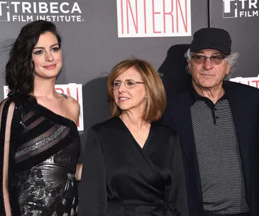 "Cast of 'The Intern' at the premiere, featuring actors and director, standing in front of a film backdrop."