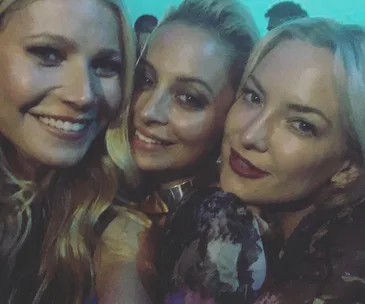 Three women taking a close-up selfie, smiling with light blue background.