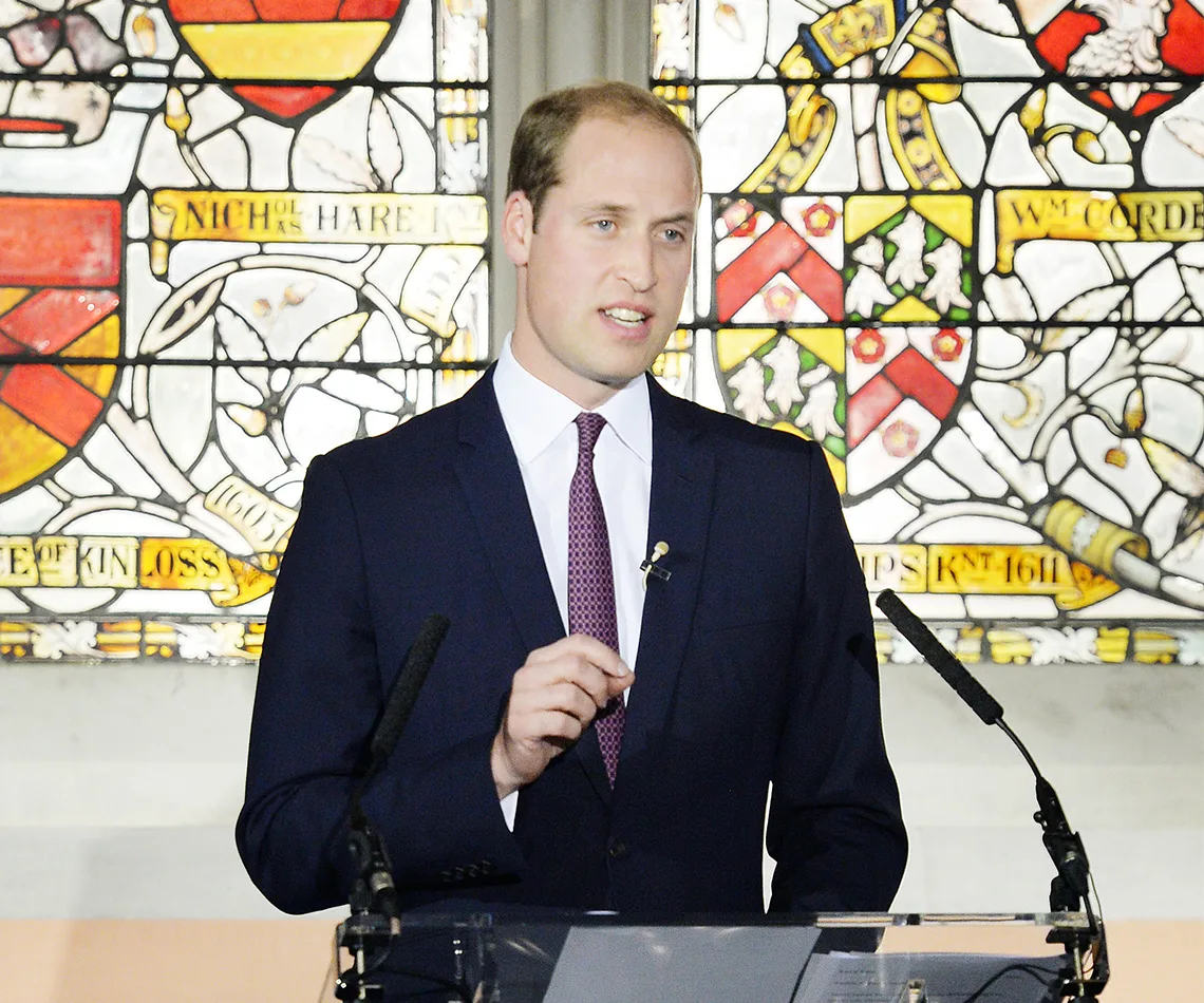 A person in a suit giving a speech in front of a stained glass window.