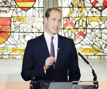 A person in a suit giving a speech in front of a stained glass window.