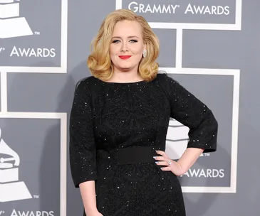 A person poses on the red carpet at the Grammy Awards, wearing a black dress with geometric patterns.