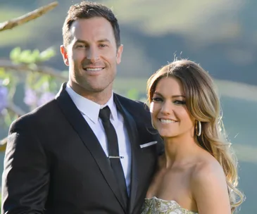 Couple dressed formally, standing outdoors, smiling at the camera.