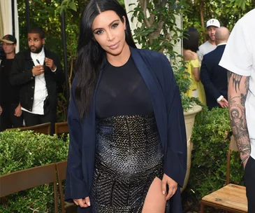 Kim Kardashian posing in an elegant outfit at an outdoor event with greenery around.