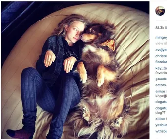 Woman lying on a bed face-to-face with a fluffy dog wearing a bow tie.
