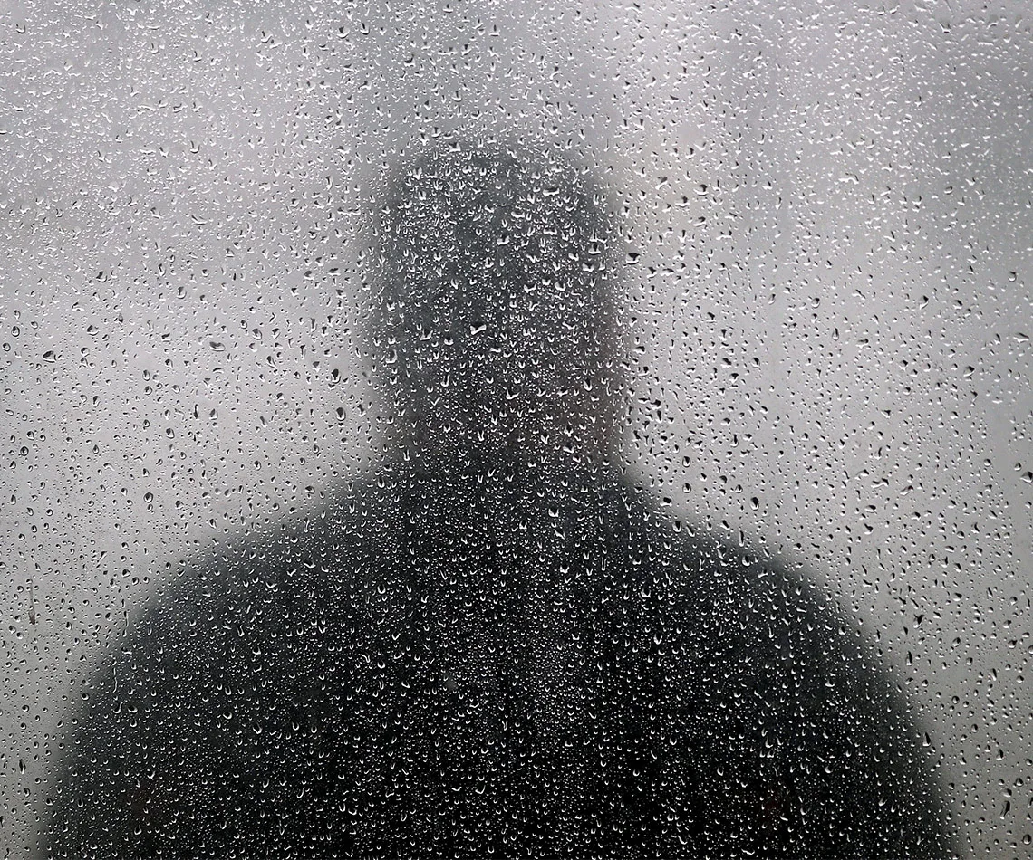 Silhouette of a person seen through a foggy, rain-covered window.