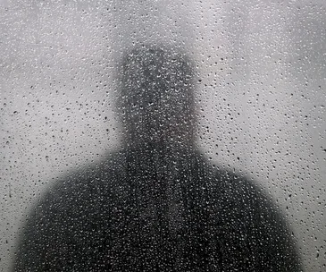 Silhouette of a person seen through a foggy, rain-covered window.