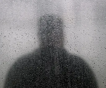 Silhouette of a person seen through a foggy, rain-covered window.