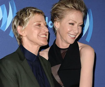 Two people smiling and embracing on a blue carpet at an event, with a backdrop featuring a circular logo.