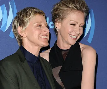 Two people smiling and embracing on a blue carpet at an event, with a backdrop featuring a circular logo.