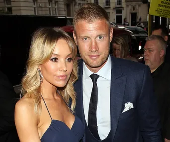 Man in suit and woman in blue dress posing at an event, surrounded by people and cars in the background.