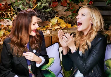 Two women sit outdoors, laughing and engaging in animated conversation, surrounded by autumn leaves.