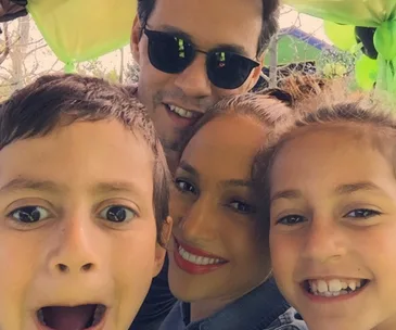 Family selfie with two adults and two children smiling under festive green decoration.