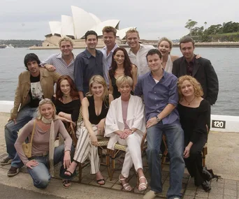 A group of people posing near a waterfront with the Sydney Opera House in the background.