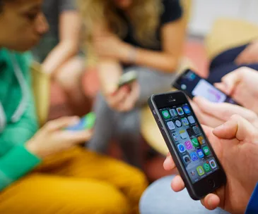 People sitting and using smartphones, focusing on apps on a phone screen in the foreground.