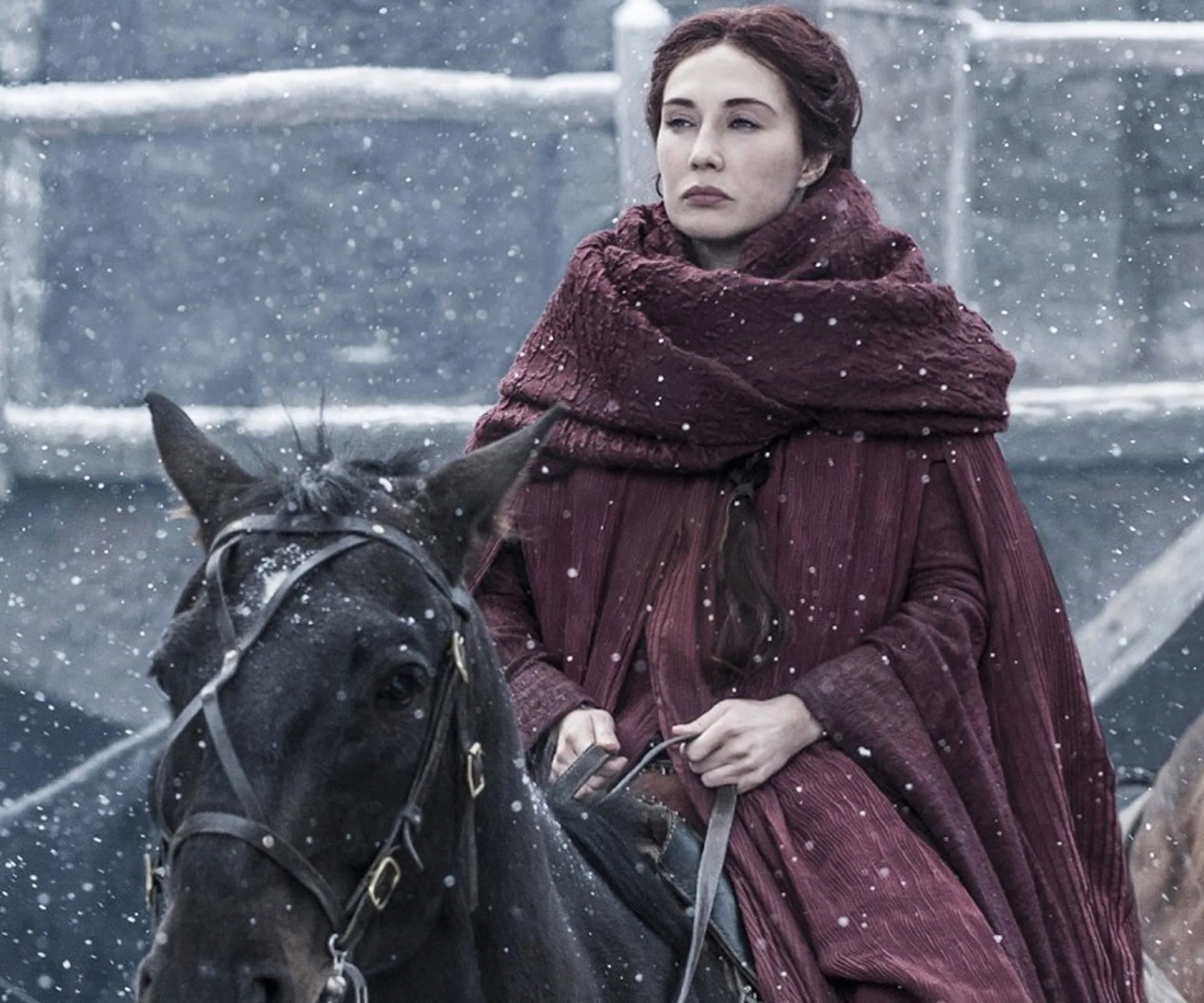 Melisandre from Game of Thrones rides a horse in a snowy setting, wearing a red cloak.
