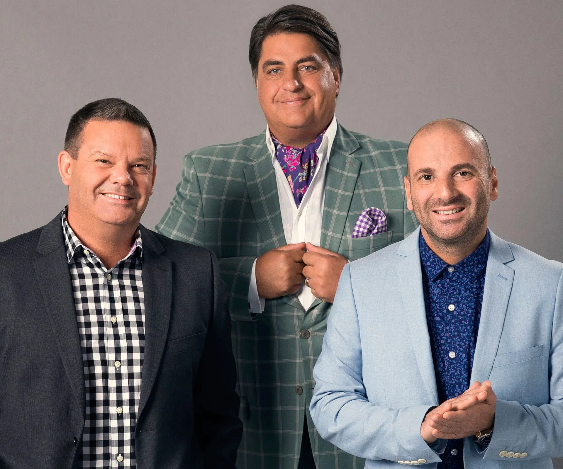 Three men in suits posing, two in the front and one behind, all smiling confidently.