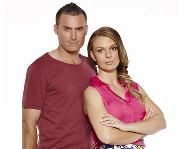 A man in a red t-shirt and a woman in a pink blouse standing close, arms crossed, posing for a photo.