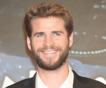 "Portrait of a smiling man with short hair and a beard, wearing a suit, against a blurred background."