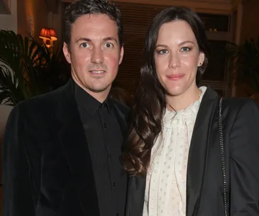 A couple poses together at an indoor event, both smiling softly at the camera.