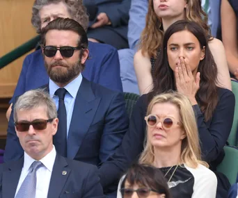 A group of people sitting at an event, focusing intently. Two in front wear sunglasses. Woman with hand near mouth in background.