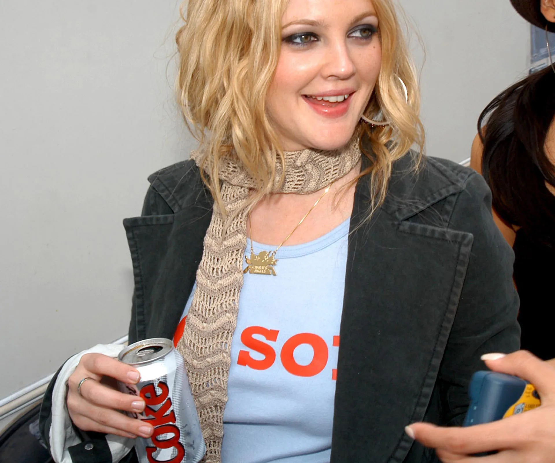 A woman smiling and holding a Diet Coke can, wearing a scarf and blue shirt.