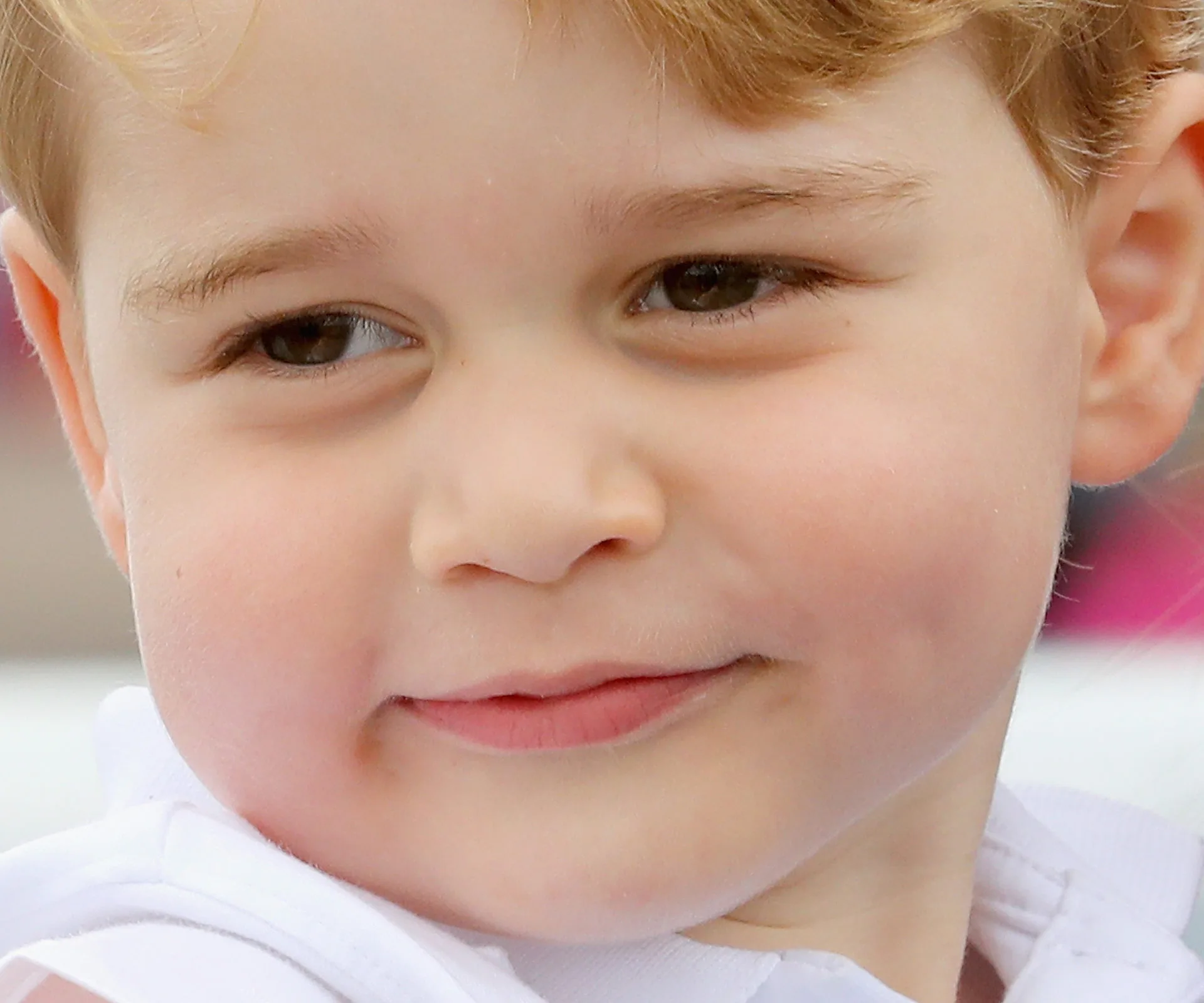 A young child with light brown hair smiles softly, wearing a white shirt.