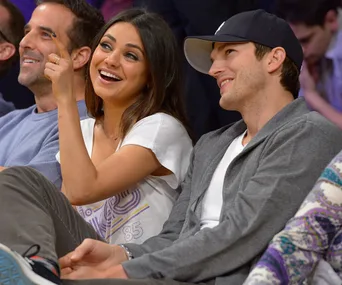 A woman and a man sitting at a sports event, smiling and looking in the same direction.
