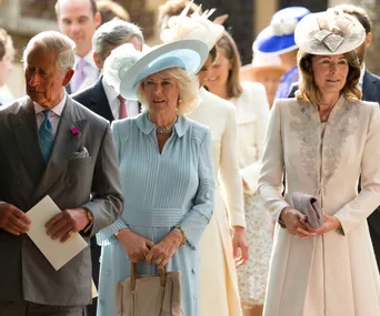 Royal family members at an outdoor event, dressed formally with hats, smiling and interacting.