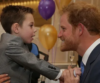 A man and a young boy smile and interact in a room with colorful balloons.