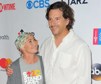 Couple smiling at cancer charity event backdrop, woman wearing headscarf, man in white shirt.
