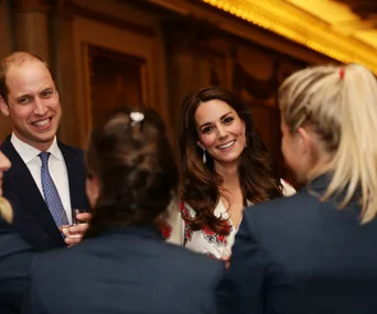 Royal couple smiling and conversing with guests in formal setting.