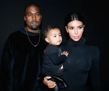 A man, woman, and child posing together wearing black clothing against a dark background.