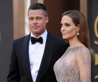 A man in a tuxedo and a woman in an embellished gown pose together on a red carpet event.