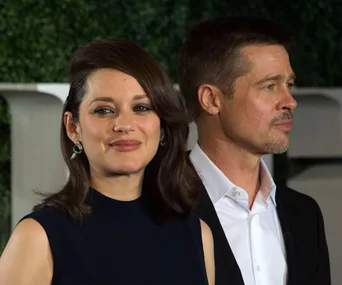 Two actors at the premiere of the movie "Allied," posing together with a foliage background.