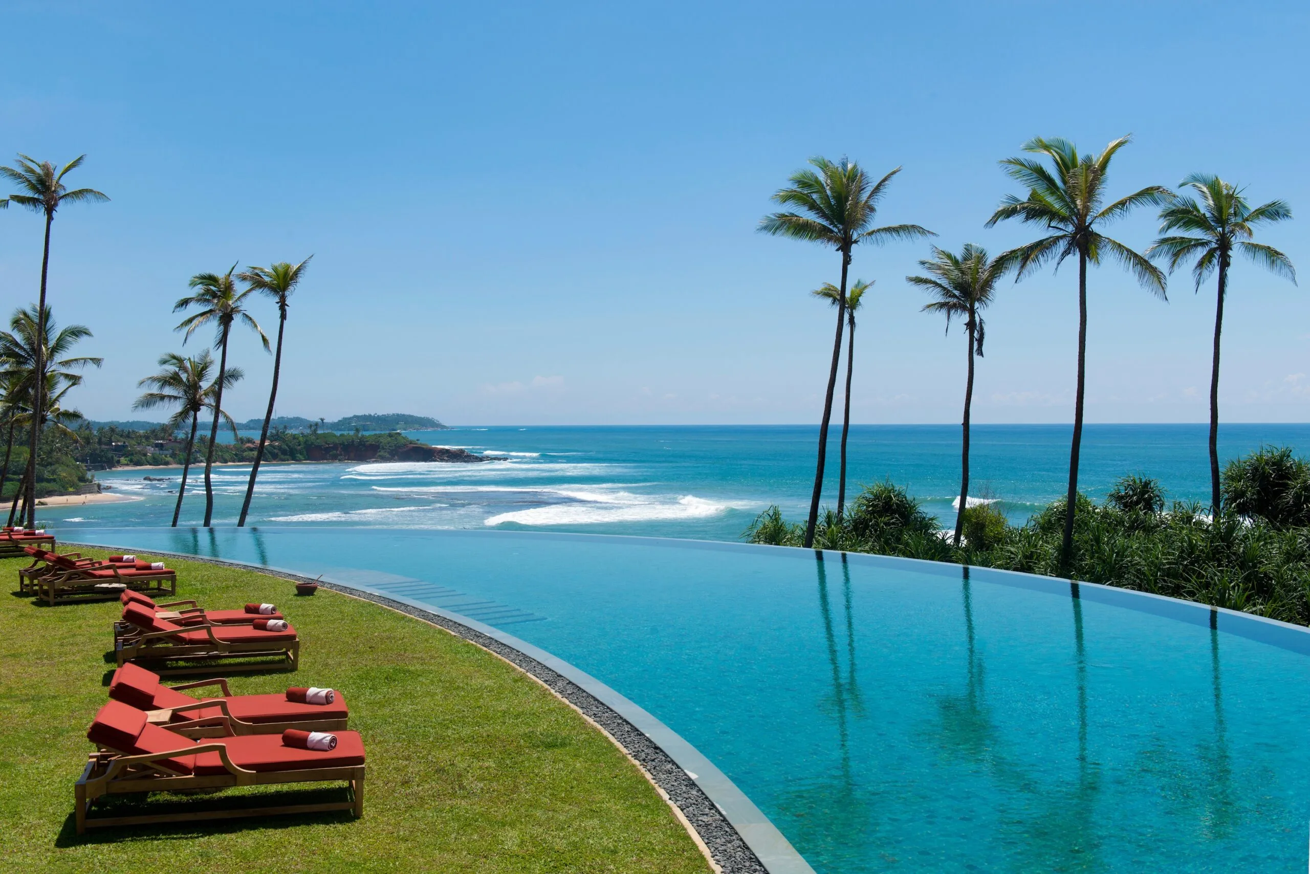 Infinity pool overlooking the ocean with palm trees and lounge chairs on a sunny day in Sri Lanka.