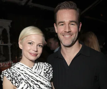 A man and woman smiling and posing together at an event, both wearing patterned and dark attire.