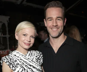 A man and woman smiling and posing together at an event, both wearing patterned and dark attire.