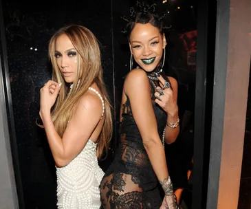 Two women posing together, one in a white pearl dress and the other in a black lace dress, smiling at an event.