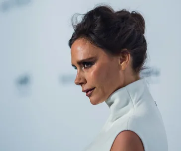Profile of a woman in a white outfit, with her hair styled up, against a plain background.