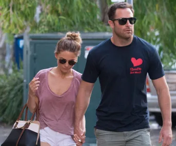 A couple walking outdoors, holding hands, both wearing sunglasses.