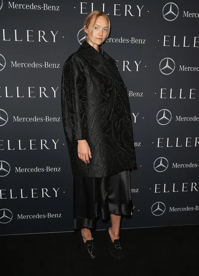 A person in a black patterned outfit poses on the red carpet at an Ellery and Mercedes-Benz event backdrop.