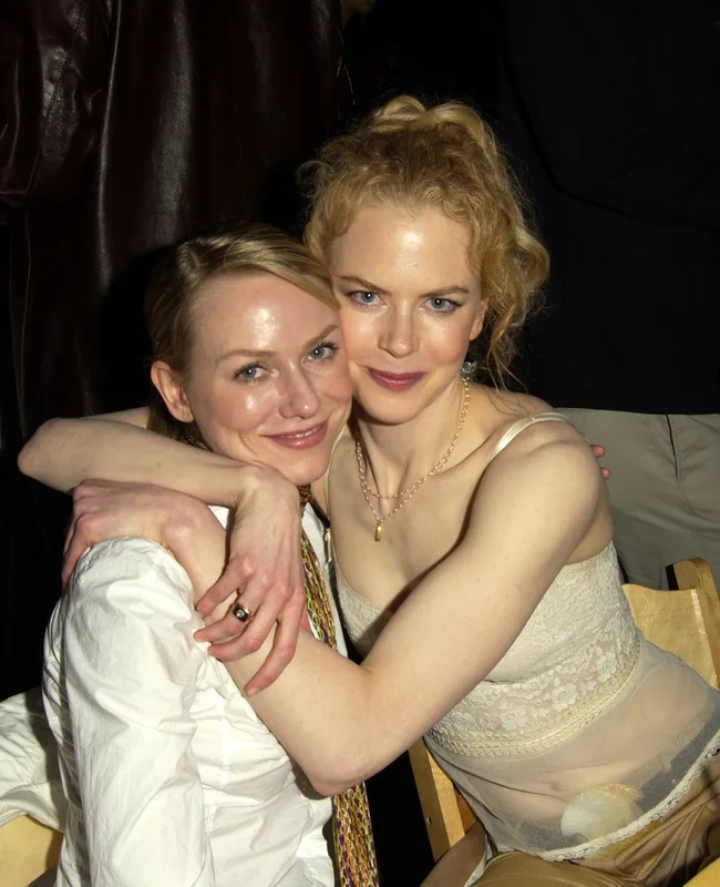 Two women sitting closely together, smiling at the camera. One woman has her arm around the other.