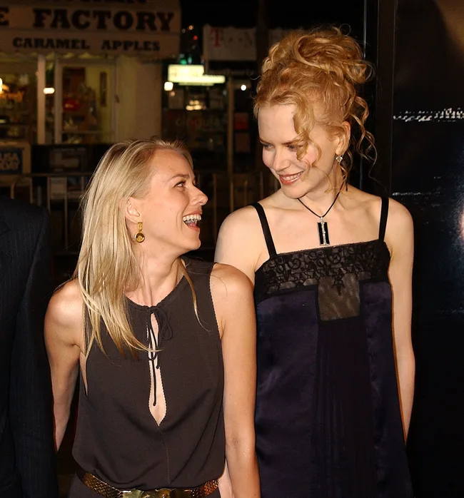 Two women smiling and looking at each other at a nighttime event, one with curly hair, the other with straight hair.