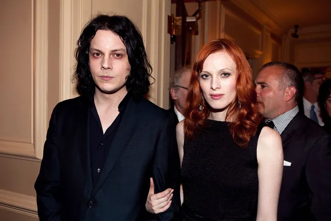 A man in a black suit and woman in a black dress pose together at an indoor event.