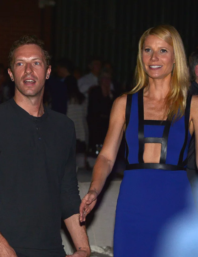 A man in a black shirt and a woman in a blue dress holding hands at a public event.