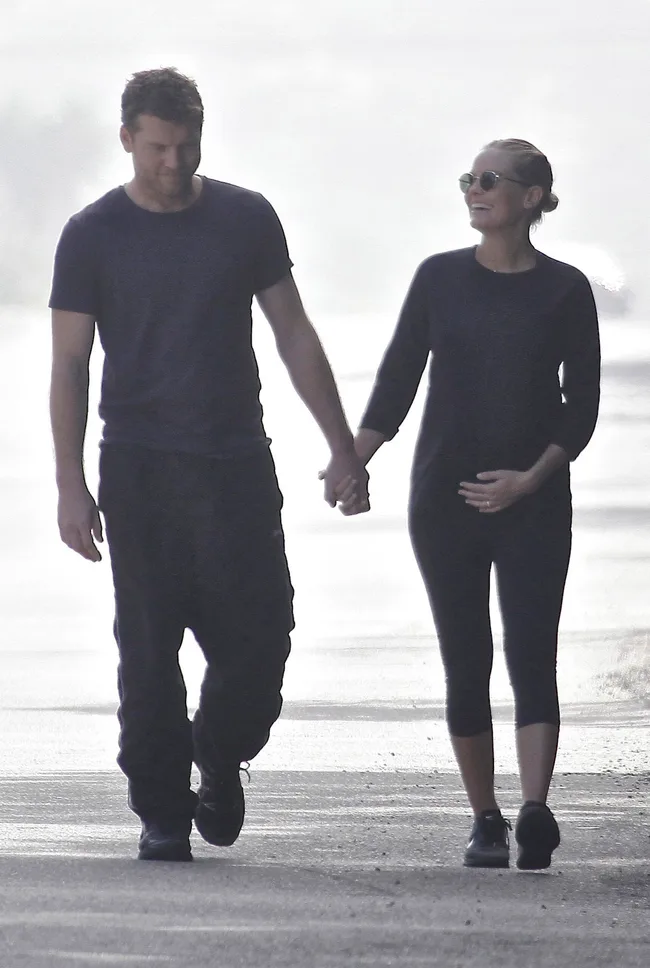Man and woman holding hands, walking outdoors; woman appears pregnant.