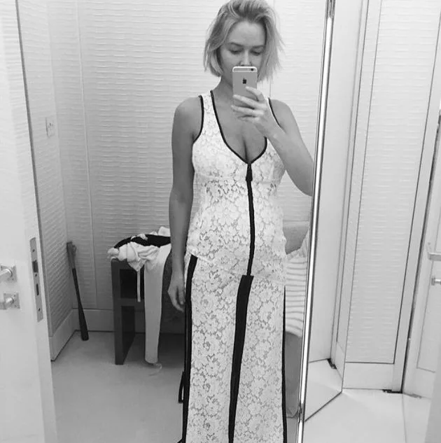 Person taking a mirror selfie in a white lace dress, in a fitting room.