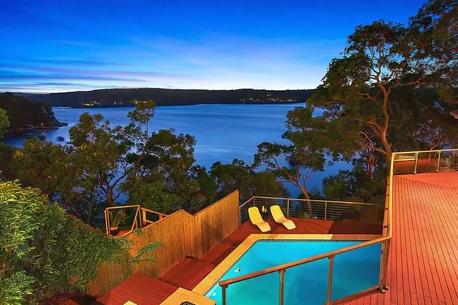 Deck overlooking a pool with two lounge chairs, surrounded by trees, and a view of a serene lake at twilight.
